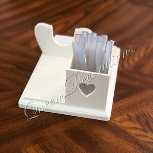 K&ouml;nnte beinhalten: Wei&szlig;er Holzorganizer mit einem herzf&ouml;rmigen Ausschnitt. Der Organizer hat ein Fach f&uuml;r Nagelspitzen und einen Halter f&uuml;r eine Nagelfeile. Der Organizer steht auf einer Holzoberfl&auml;che.