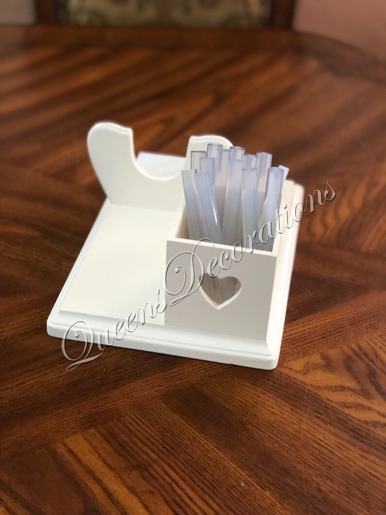 K&ouml;nnte beinhalten: Wei&szlig;er Holzorganizer mit einem herzf&ouml;rmigen Ausschnitt. Der Organizer hat ein Fach f&uuml;r Nagelspitzen und einen Halter f&uuml;r eine Nagelfeile. Der Organizer steht auf einer Holzoberfl&auml;che.