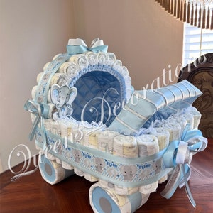 May include: A blue and white diaper cake shaped like a baby carriage. The carriage is decorated with a blue ribbon, a white lace trim, and a small stuffed elephant. The wheels of the carriage are made of rolled up diapers.