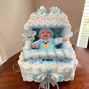 May include: A blue and white diaper cake shaped like a baby carriage with a baby doll inside. The carriage is decorated with blue and white ribbons and a silver glitter pillow.