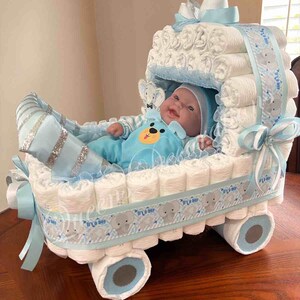 May include: A blue and white diaper cake shaped like a baby carriage with a baby doll inside. The carriage is decorated with a blue ribbon and a gray ribbon with the words "It's a Boy" printed on it. The wheels are made of rolled up diapers.