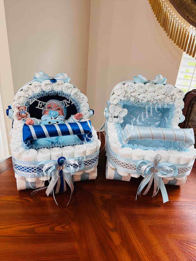Puede incluir: Dos carritos de pastel de pa&ntilde;ales azules y blancos decorados con cinta azul y plateada. Un carrito tiene un mu&ntilde;eco.
