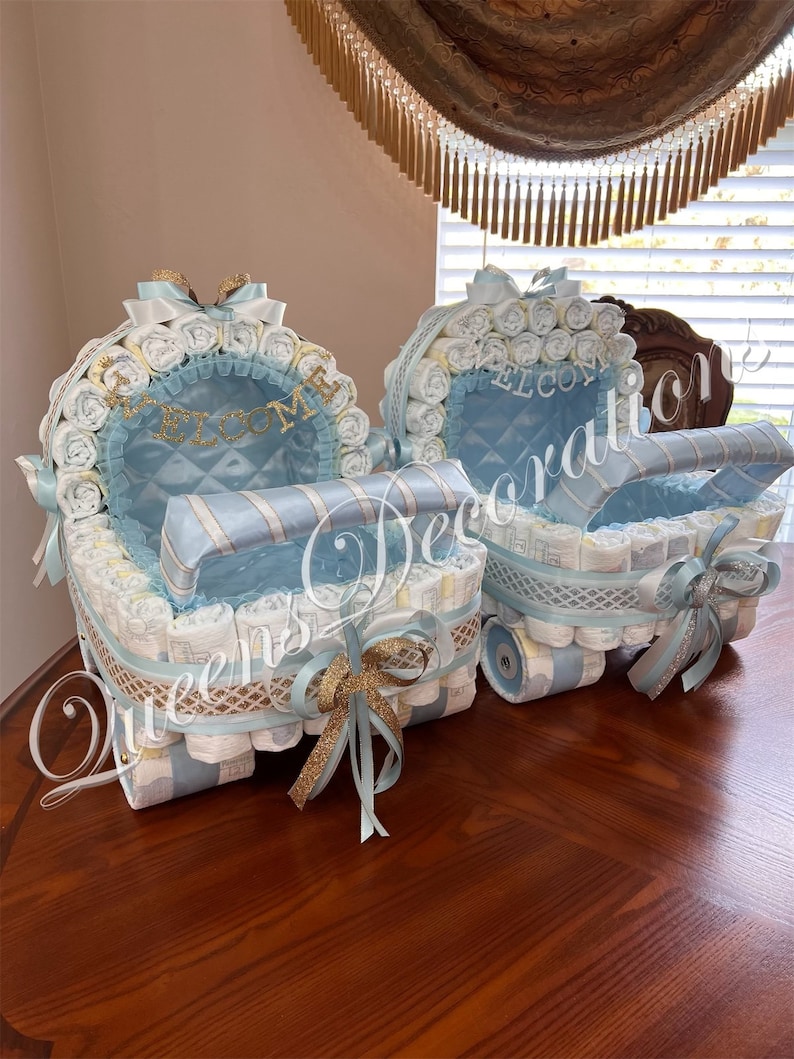 Puede incluir: Dos cochecitos de pastel de pa&ntilde;ales azul y blanco decorados con cinta dorada y la palabra "Bienvenido".