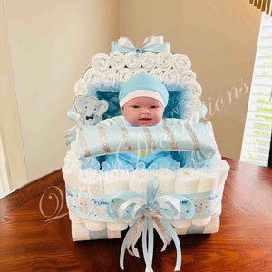May include: A blue and white diaper cake shaped like a baby carriage. The cake is decorated with a blue ribbon and a silver bow. A baby doll is sitting in the carriage.
