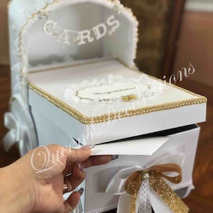 May include: White baby carriage card box with gold trim and a white ribbon with gold polka dots. The box has a sign that says "Cards" on the top.