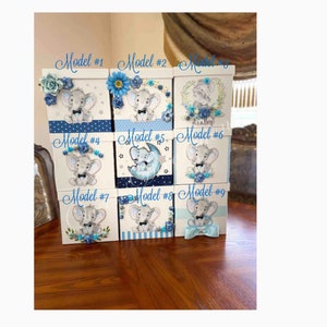 May include: Nine different designs of small, white gift boxes with blue and white decorations. Each box features a cartoon elephant with different designs, including stars, a moon, and a bow tie. The boxes are labelled with numbers 1 through 9.