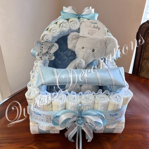 May include: A blue and white diaper cake shaped like a baby carriage with a gray elephant plush toy sitting inside. The cake is decorated with a blue and white ribbon and a small white tag that says "Kelly baby".