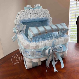 May include: A blue and white diaper cake shaped like a baby carriage. The carriage is decorated with a silver ribbon and a blue bow. The cake is made of diapers, rolled up and stacked. It is a baby shower gift.