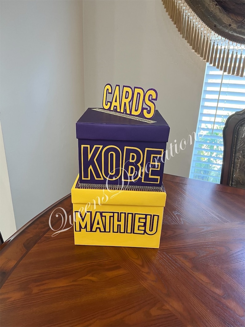K&ouml;nnte beinhalten: Zwei &uuml;bereinander gestapelte Kartons f&uuml;r Karten, der obere Karton ist lila mit dem Wort "CARDS" in gelben Buchstaben, der untere Karton ist gelb mit den Worten "KOBE MATHIEU" in lila Buchstaben.