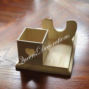 K&ouml;nnte beinhalten: Holz-Schreibtisch-Organizer mit einem quadratischen Fach und einem gebogenen Halter. Der Organizer hat einen herzf&ouml;rmigen Ausschnitt und der Text "Queens Decorations" ist an der Seite sichtbar.