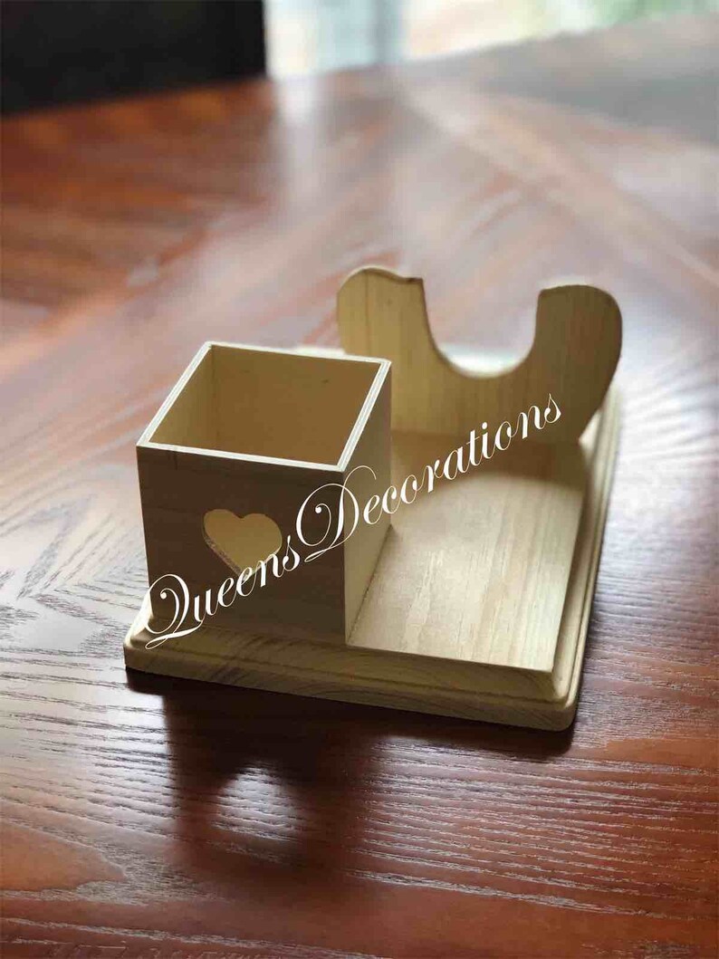 K&ouml;nnte beinhalten: Holz-Schreibtisch-Organizer mit einem quadratischen Fach und einem gebogenen Halter. Der Organizer hat einen herzf&ouml;rmigen Ausschnitt und der Text "Queens Decorations" ist an der Seite sichtbar.