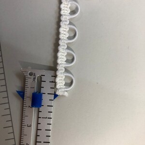 May include: White elastic trim with small loops, measured with a ruler in inches.
