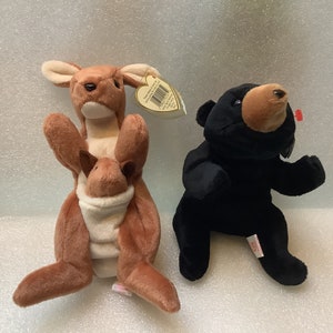 May include: Two plush toys, a brown kangaroo with a joey in its pouch and a black bear. Both toys have red and white Ty tags.