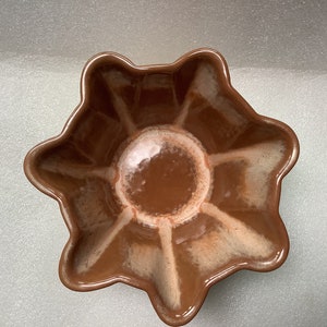 Può includere: Una ciotola in ceramica marrone con un design a stella. La ciotola ha una glassa bianca che crea un effetto marmorizzato.