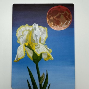 May include: A rectangular art print depicting a white and yellow iris flower with a red and brown moon against a blue sky. The flower has green stems and leaves. The background fades from dark blue to light blue.