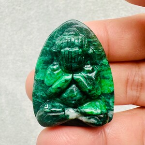 May include: A green jade carving of a meditating Buddha, with the hands in a prayer position. The carving is detailed and intricate, with a smooth, polished finish.