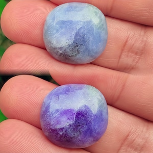 Puede incluir: Dos piedras preciosas pulidas y redondeadas. La piedra superior es una mezcla de tonos azules, grises y blancos. La piedra inferior es una mezcla de morado, blanco y gris. Ambas piedras tienen un acabado liso y brillante.