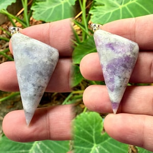 Puede incluir: Dos colgantes plateados con forma triangular. Los colgantes están hechos de cristal blanco y morado con una superficie texturizada.