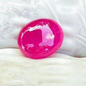 Pode incluir: Um cabochão de gema rosa vibrante com uma superfície lisa e polida.
