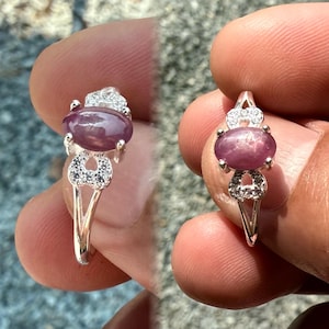 Puede incluir: Un anillo de plata con una piedra ovalada púrpura rodeada de piedras blancas más pequeñas. El anillo tiene un diseño delicado e intrincado.