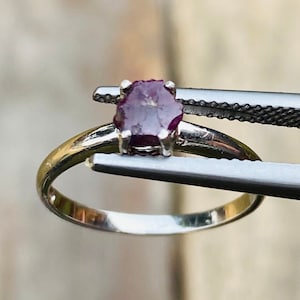 May include: A silver ring with a purple gemstone set in a prong setting.