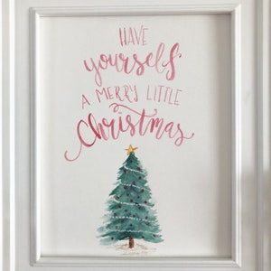 May include: A framed watercolour painting. The artwork displays the text "Have yourself a Merry Little Christmas" in pink script above a green Christmas tree decorated with red baubles and a gold star.
