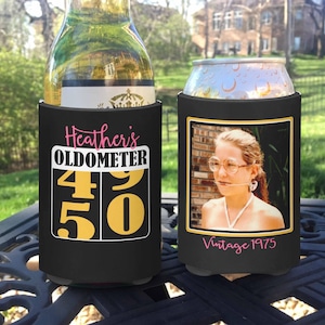 May include: Two black beverage insulators. One features the text "Heather's OLDOMETER" with the numbers 49 and 50 in gold. The other displays a vintage photo with the text "Vintage 1975" in pink.