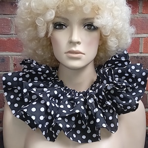 May include: A black and white polka dot ruffled collar. The collar is made of a dark fabric with white polka dots. The ruffles are gathered around the neckline. The collar is a costume accessory.