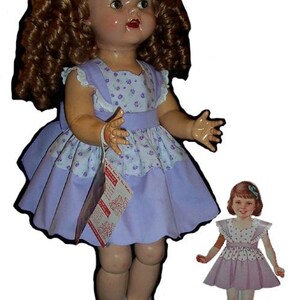 May include: A vintage doll with curly brown hair, wearing a lilac dress with a floral bodice and matching paper doll. The doll has a tag attached. The doll is wearing black shoes and white socks.