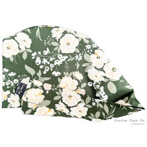 May include: Green scrub cap with a white floral pattern and a black label that says "Custom Caps Co."