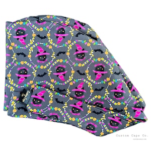 May include: Gray surgical scrub cap with a Halloween-themed pattern. The pattern includes black cats wearing pink witch hats, bats, candy corn, and other festive elements. The cap has a matching band and the text "Custom Caps Co."