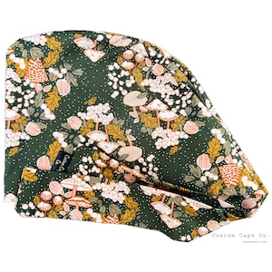 May include: A dark green surgical scrub cap with a repeating pattern of mushrooms, leaves, and flowers in shades of orange, white, and pink. The cap has a tag that says "Custom Caps Co."