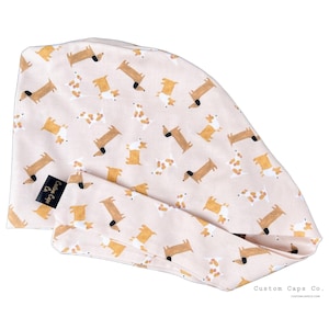 Könnte beinhalten: Hellrosa OP-Haube mit einem sich wiederholenden Muster aus braunen und weißen Dackeln. Die Haube hat ein passendes Stirnband und ein schwarzes Etikett mit "Custom Caps Co."