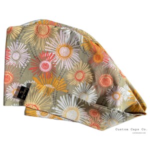 Puede incluir: Un gorro de quirófano de color verde, amarillo, naranja y blanco con estampado floral y el texto "Custom Caps Co." en la esquina inferior derecha.