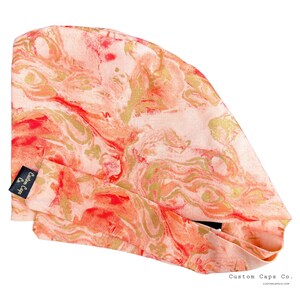 May include: A pink and gold marble print surgical cap with a black label that says "Custom Caps Co."