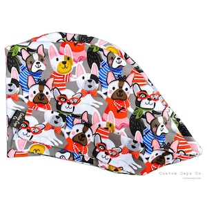 May include: A grey and white patterned surgical cap with a repeating design of cartoon French Bulldogs wearing sunglasses, bow ties, and other accessories. The cap has a label that reads "Custom Caps Co."