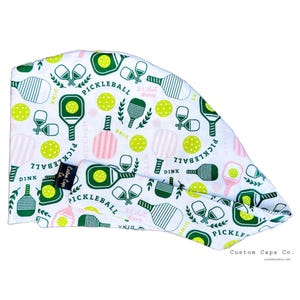 May include: White scrub cap with a repeating pattern of pickleball paddles, balls, and text. The design includes green, pink, and white elements. The text includes "Pickleball", "Dink", and "3rd shot drive".