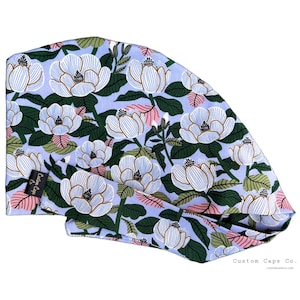 Könnte beinhalten: Eine blaue und weiße OP-Mütze mit Blumenmuster und einem rosafarbenen Akzent. Die Mütze trägt den Text "Custom Caps Co." und "customcapsco.com" auf der Unterseite.