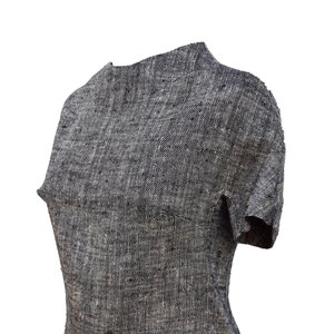 May include: A gray and black textured short-sleeve top. The top has a high neckline and a fitted silhouette. The fabric appears to be woven, with a subtle pattern. The garment is displayed on a mannequin, showcasing its shape and design.