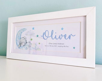 May include: A white frame with a blue and green watercolor illustration of a teddy bear sleeping on a crescent moon. The illustration is surrounded by stars and clouds. The text "Oliver James Anderson Born on 10th July 2021, weighing 4lbs 8oz" is printed below the illustration.