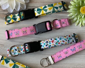 May include: Five colorful dog collars with different patterns, including butterflies, flowers, and geometric shapes. The collars are made of fabric and have adjustable buckles.