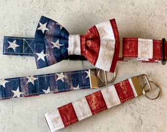 May include: A set of three patriotic accessories featuring a bow tie, a key chain, and a collar. All three items are made of fabric with a distressed American flag design in red, white, and blue.