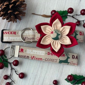 May include: A beige and brown dog collar with a red and beige flower charm. The collar has a repeating pattern of reindeer and the words "Dancer, Blitzen, Donner, Vixen, Comet, Cupid".