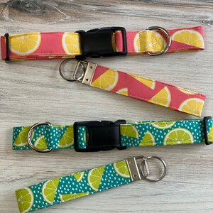 May include: Two sets of matching dog collars and leashes with a lemon print. One set is pink with yellow lemons, the other is teal with green lemons. Both sets have black buckles and silver D-rings.