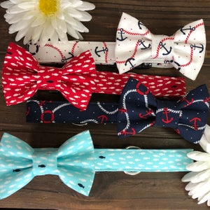 May include: A collection of nautical-themed bow ties in various colors and patterns. Designs include anchors, fish, and rope details. The bow ties are red, white, and blue, with a light blue option. The bow ties are for pets.