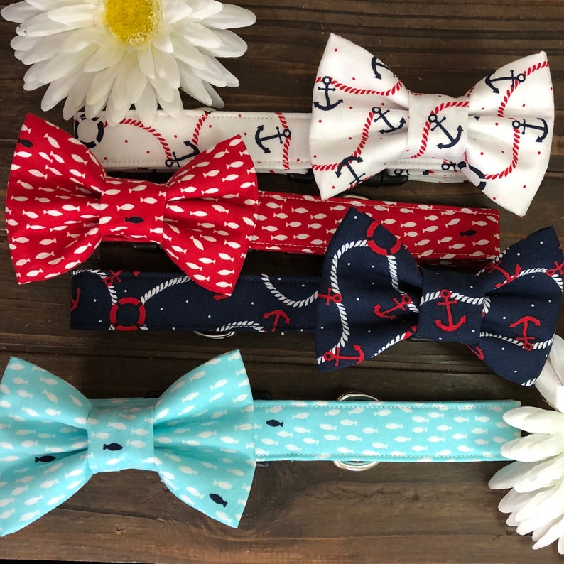 May include: A collection of nautical-themed bow ties in various colors and patterns. Designs include anchors, fish, and rope details. The bow ties are red, white, and blue, with a light blue option. The bow ties are for pets.