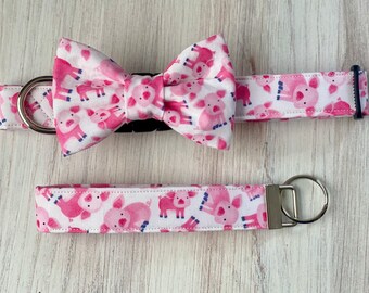 May include: Pink and white dog collar and matching bow tie with a pattern of pink pigs. The collar has a silver buckle and a silver key ring.