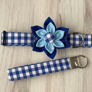 May include: Blue and white gingham dog collar with a blue flower accent. The collar has a silver D-ring and a matching leash.