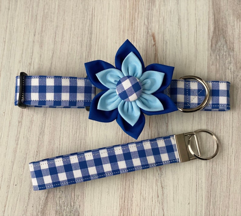 May include: Blue and white gingham dog collar with a blue flower accent. The collar has a silver D-ring and a matching leash.