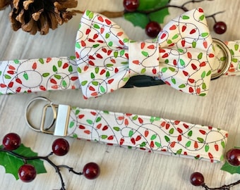 May include: A white dog collar, bow tie, and wristlet with a repeating pattern of red and green Christmas lights. The bow tie is pre-tied. The wristlet has a silver metal ring.
